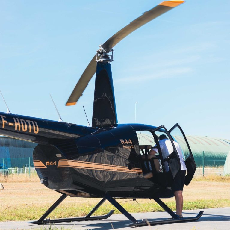 Photo d'un hélicoptère R44 blanc vue de trois quart face avec un grand ciel bleu